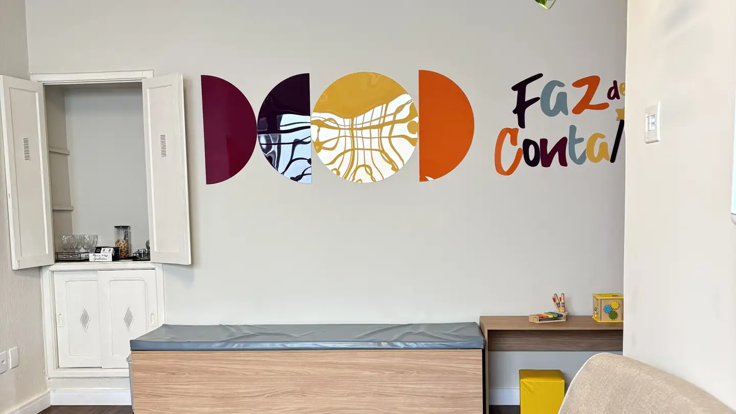 Recepção da Clínica Faz de Conta, com sofá claro, bancos e o logotipo colorido na parede