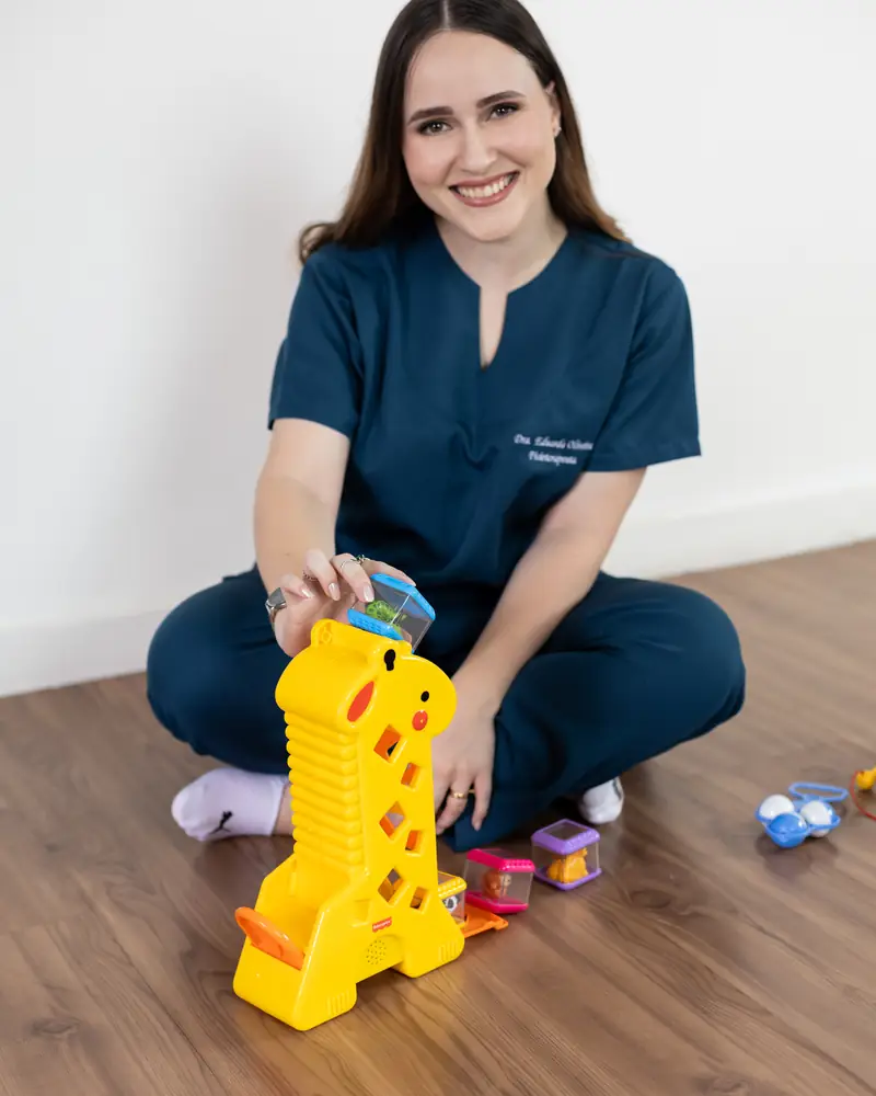 Fisioterapeuta sentada no chão da sala com brinquedos de encaixe