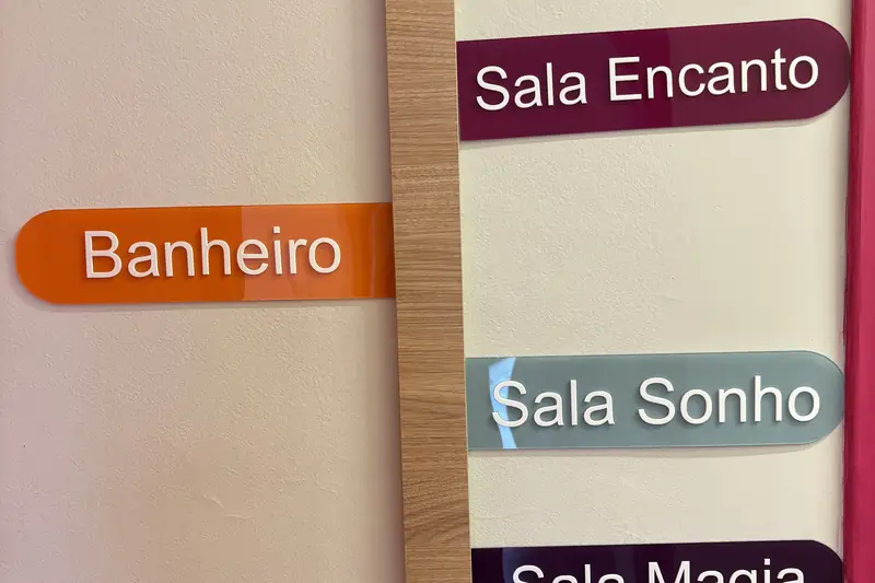Placa de sinalização da clínica indicando o banheiro e as salas Encanto, Sonho e Magia