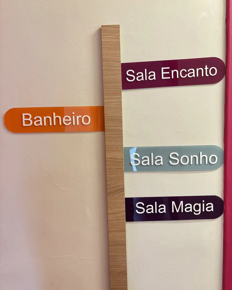 Placa indicando o banheiro e as salas Encanto, Sonho e Magia